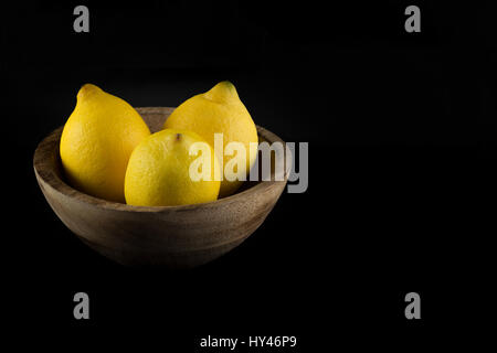 I limoni in una naturale fatta a mano in vero legno ciotola isolato in sfondo nero Foto Stock