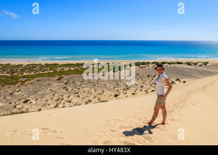 Giovane donna in piedi sulla duna di sabbia sulla spiaggia di Sotavento sulla Penisola di Jandia e guardando oceano, Fuerteventura, Isole Canarie, Spagna Foto Stock