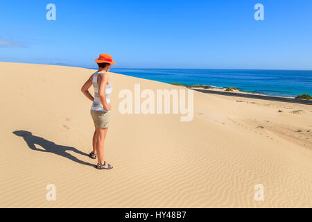Giovane donna tourist permanente sulla duna di sabbia in Corralejo National Park e guardando oceano, Fuerteventura, Isole Canarie, Spagna Foto Stock