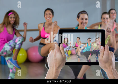 Ritagliato mano azienda digitale compressa contro un gruppo di donne di eseguire aerobica Foto Stock