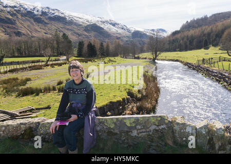 Scena retroilluminata di pensionata attiva donna in San Giovanni in Valle con Snow capped Helvellyn in background, Cumbria, England, Regno Unito Foto Stock