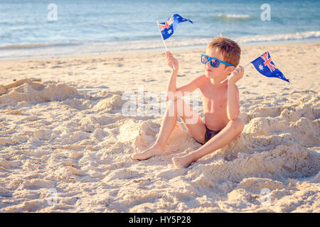 Carino sorridente ragazzo seduto sulla spiaggia e azienda Australian flag su Australia day Foto Stock