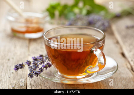 Il tè di lavanda in un bicchiere di vetro, miele, lavanda fiori sul vecchio sfondo di legno Foto Stock