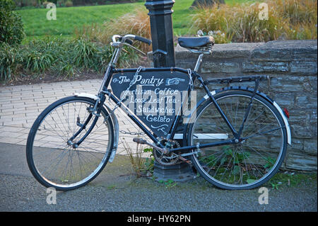 Un vecchio nero bicicletta incatenato ad un lampione e poggiante contro una parete di pietra. Foto Stock