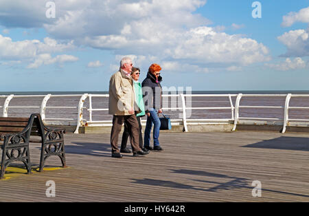 Una vista di tre persone che passeggiano sul molo a Cromer, Norfolk, Inghilterra, Regno Unito. Foto Stock