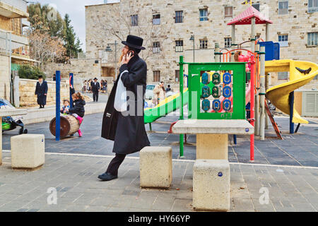 Gerusalemme, Israele - 29 dicembre 2016: ebrea ortodossa Uomo con telefono mobile a piedi alla strada presso il parco giochi nel quartiere ebraico. Foto Stock