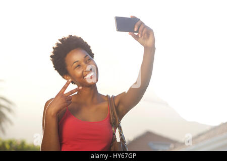 Close up ritratto di una giovane e bella donna africana gesti segno di pace mentre prendendo un selfie Foto Stock