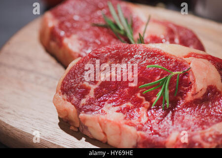 Carne di manzo crudo su un tagliere con le spezie e gli ingredienti per cucinare. Foto Stock