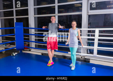 Sorridente giovane coppia sportiva nell'abbigliamento sportivo in appoggio dopo allenamento regolari di pugilato ring in una palestra Foto Stock