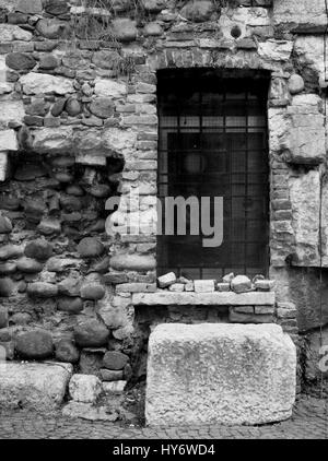 Oldamaged e riparato un muro di mattoni con una finestra sbarrata e vecchie pietre in monocromia Foto Stock