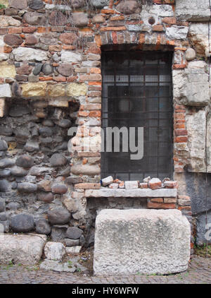 Oldamaged e riparato un muro di mattoni con una finestra sbarrata e vecchie pietre Foto Stock