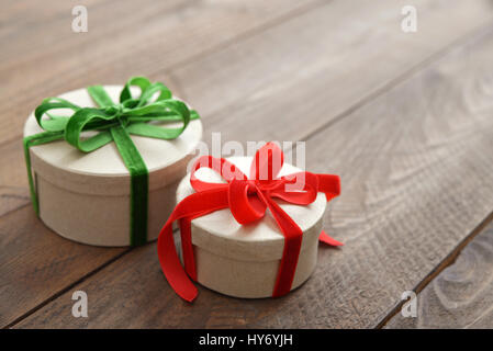 Round confezioni regalo con il rosso e il verde nastri su sfondo di legno Foto Stock