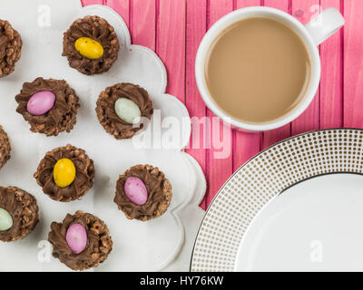 Pasqua croccante di cioccolato nidi di cereali con mini uova di pasqua contro un sfondo rosa Foto Stock