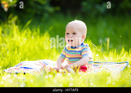 Adorable baby boy eating apple giocando sul manto colorato in verde erba. Bambino divertirsi sulla famiglia picnic nel giardino estivo. I bambini mangiano la frutta. Un sano Foto Stock