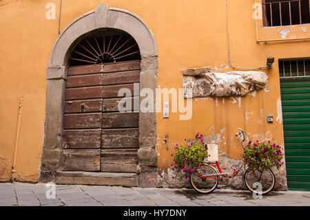 Red moto caricata con fiori in piedi di fronte ad una vecchia porta di legno in un tradizionale italiano centro medievale della città. Toscana, Italia. Foto Stock