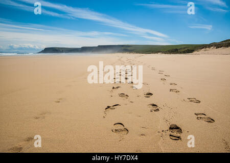 Impronte di scarpe da trekking sulla sabbia di una spiaggia remota in Scozia, Regno Unito. Montagne, oceano e cielo blu in background. Foto Stock