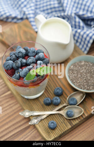 Il budino con semi di Chia, yogurt e frutti di bosco freschi in vetro su sfondo di legno Foto Stock