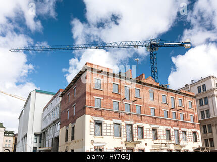 Il vecchio edificio in mattoni sotto la ricostruzione con la costruzione di gru sul cielo blu sullo sfondo Foto Stock