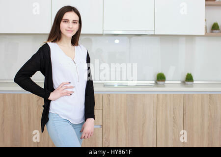 Piuttosto giovane donna con i capelli neri in piedi in cucina e sorridente Foto Stock