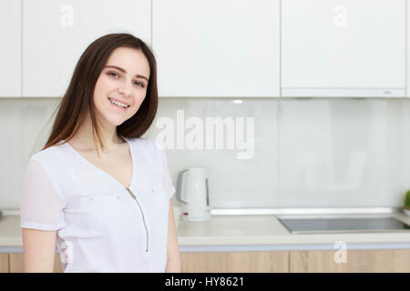 Piuttosto giovane donna con i capelli neri in piedi in cucina e sorridente Foto Stock