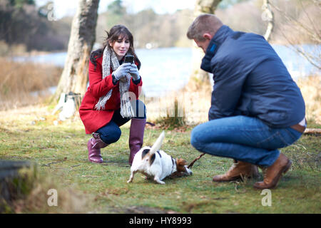 Una donna prende una fotografia del suo cane durante una passeggiata nel bosco Foto Stock