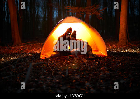 Un paio di sedersi in una tenda di notte con i loro cani e guardare il proprio laptop Foto Stock
