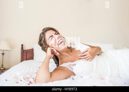 Una sposa di ridere mentre posa sul letto nella sua suite nuziale Foto Stock