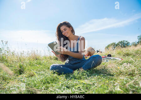 Una giovane donna legge un libro mentre seduto in un prato Foto Stock