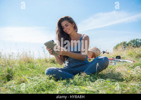 Una giovane donna legge un libro mentre seduto in un prato Foto Stock