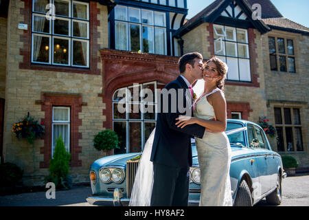 La sposa e lo sposo di condividere un bacio nel giorno del matrimonio come l'auto nozze li attende Foto Stock