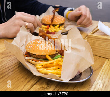 L'uomo mangiare hamburger con pancetta affumicata con patate fritte e bere il tè. Street fast food. Foto Stock