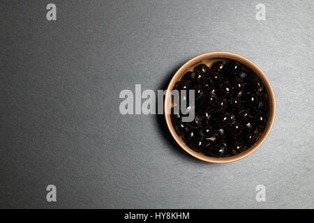 Vista superiore: tazza di olive nere su fondo nero rustico in pietra ardesia con spazio di copia Foto Stock