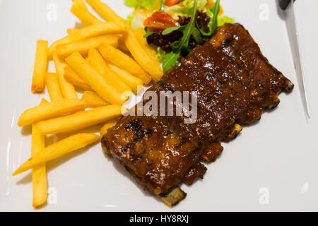 Costolette di maiale bistecca patatine fritte e verdure su piastra bianca arrosto affettata barbecue costolette di maiale, focus sulla carne tagliata a fettine Foto Stock