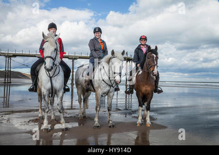 Tre donne a cavallo a Saltburn spiaggia su una luminosa giornata di sole Foto Stock