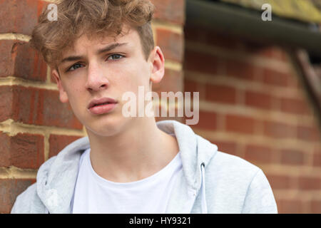 Maschio serio ragazzo adolescente fuori appoggiato su di un muro di mattoni di indossare una felpa con cappuccio grigio Foto Stock