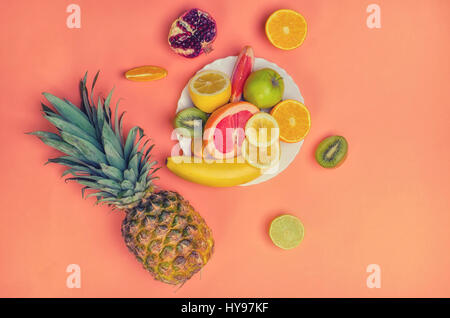 Delizioso mix di frutta con ananas, arancio, calce, kiwi, banana, melograno su vintage sfondo arancione. Parte superiore di vista. Foto Stock