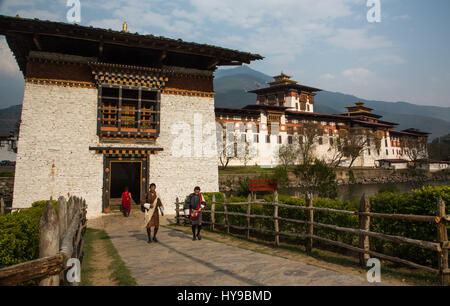 Uomini bhutanesi in ghos tradizionale presso il gate bridge house e il Punakha Dzong. Punakha, Bhutan. Foto Stock