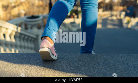 Giovane ragazza è al piano di sotto a piedi sulla scaletta. Step-down. Indossa sneakers. business o il concetto di istruzione Foto Stock