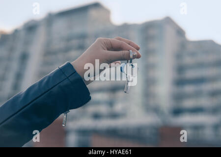 Mano che tiene la chiave con un moderno edificio di sfondo. Acquisto di nuova casa o appartamento concetto. Foto Stock