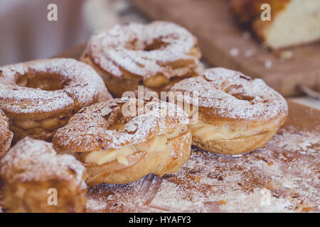 Pane appena sfornato profiteroles riempito con crema alla vaniglia e coperto con mandorle tostate e zucchero in polvere di legno rustico bordo, close up Foto Stock