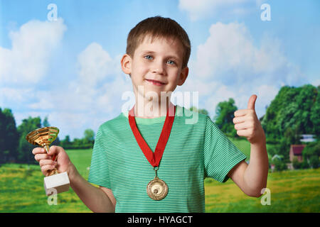 Ragazzo sportivo vincitore con la coppa e medaglia su sfondo natura Foto Stock