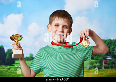 Ragazzo sportivo vincitore con la coppa e medaglia su sfondo natura Foto Stock