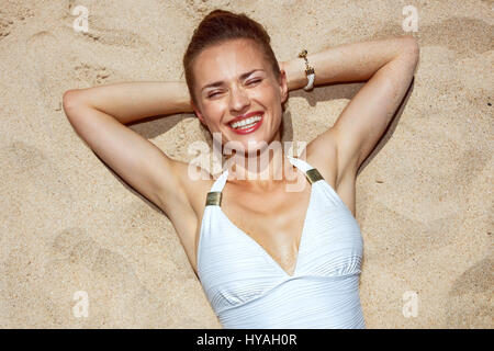 Calda sabbia di trattamento. Donna sorridente in costume da bagno la posa sulla sabbia Foto Stock