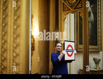 Un membro del personale può contenere un metro di Londra segno presentato alla Regina Elisabetta II durante la sua visita alla stazione della metropolitana di Aldgate East nel 2010, durante un'anteprima per la mostra di Royal doni, che è parte della stagione estiva con apertura delle camere di stato a Buckingham Palace di Londra. Foto Stock