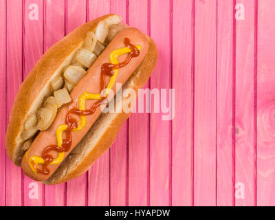 Hot Dog in un panino con cipolle fritte ketchup e senape contro un sfondo rosa Foto Stock