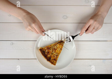 Mani femminili il taglio di un pezzo di torta su una piastra bianca. Vista superiore Foto Stock