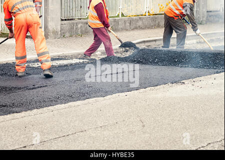 Operai edili nel corso di asfaltatura lavori stradali indossando tute. Il lavoro manuale sul sito in costruzione. Foto Stock