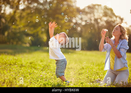 Capretto maschio con la madre avendo divertimento cattura bolle di sapone Foto Stock