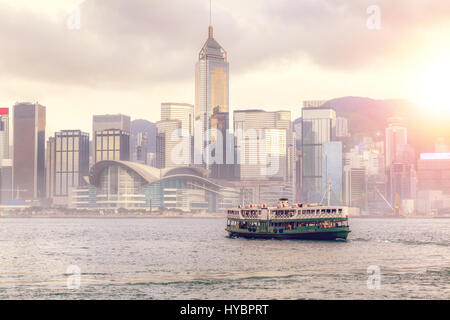 Nel tardo pomeriggio tramonto sulla skyline di Hong Kong con nave traghetto attraversando il Victoria Harbour da Tsim Sha Tsui. La deliberata lens flare e rendering HDR. Foto Stock