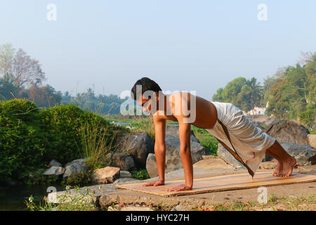 Uomo indiano a praticare yoga accanto a un fiume in India del Sud. Foto Stock